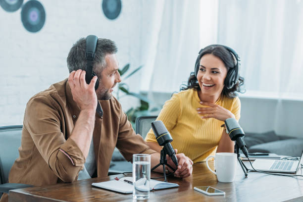 Two podcast hosts wearing headphones, laughing together at a microphone-equipped desk