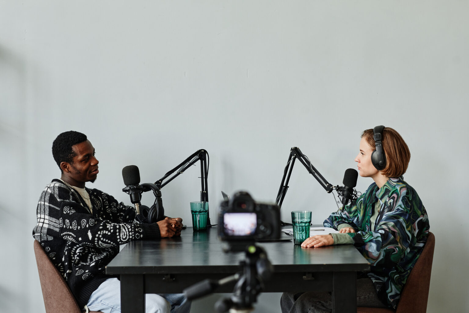 Two people recording an interview at a table with a camera on a tripod in the foreground