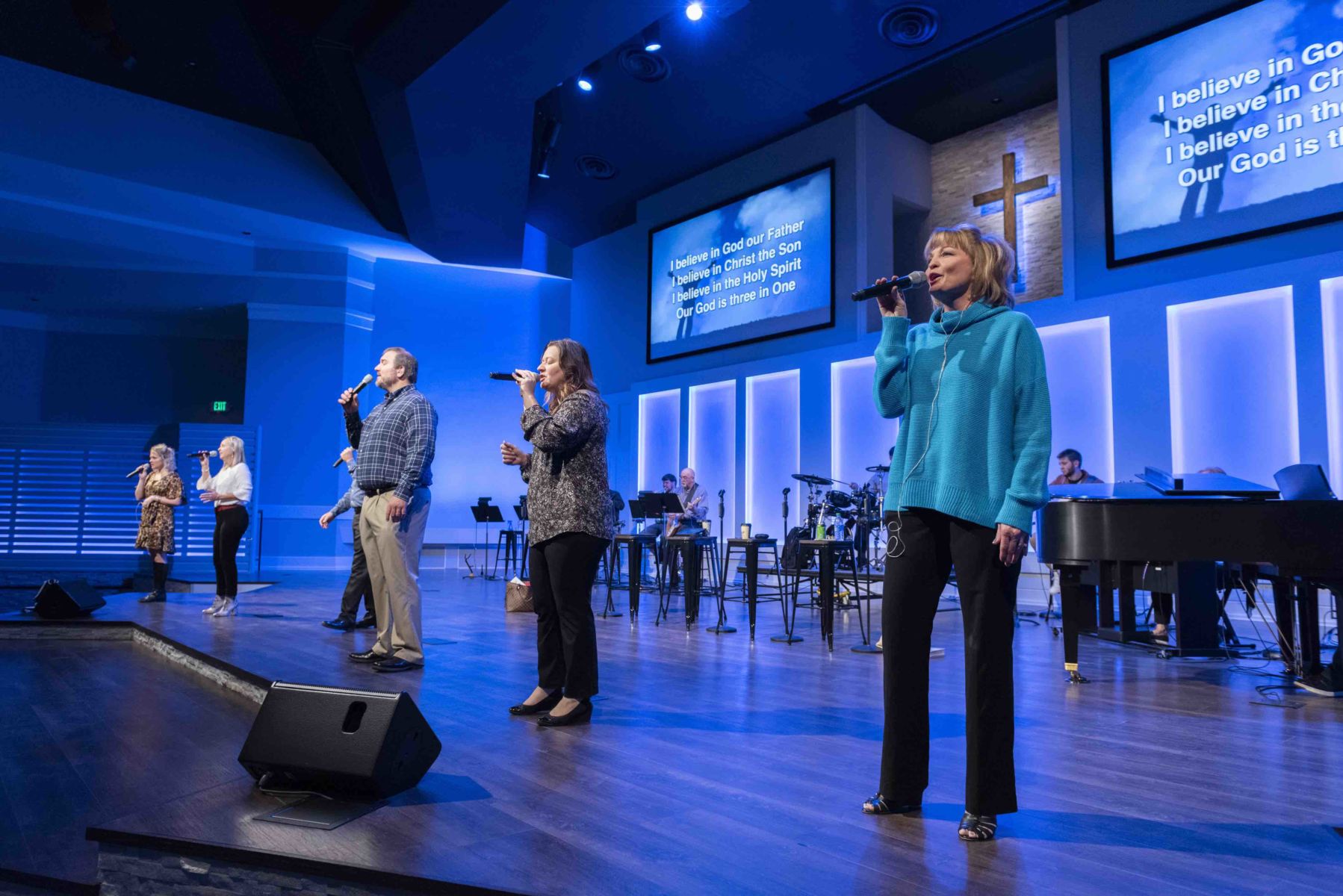 A church worship team performing on stage with singers and musicians, lyric screens overhead